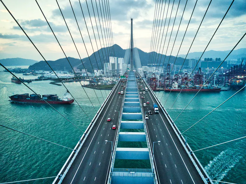 Traffic crossing a cable-stayed bridge above a harbour with cargo ships and cranes