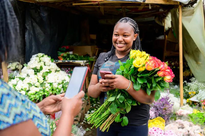 A flower seller and a customer holding mobile phones at a flower stall