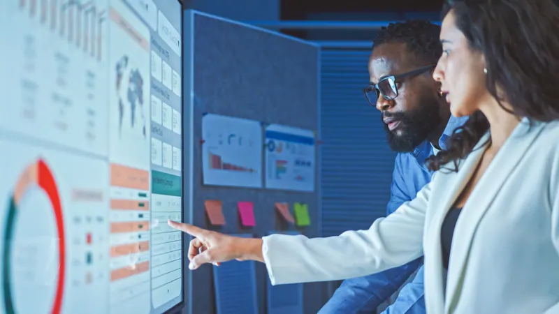 Two analysts reviewing charts and research data on a large screen
