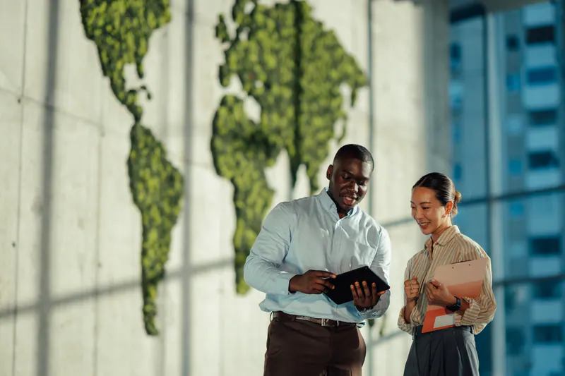 Two colleagues discussing information on a tablet in front of a world map