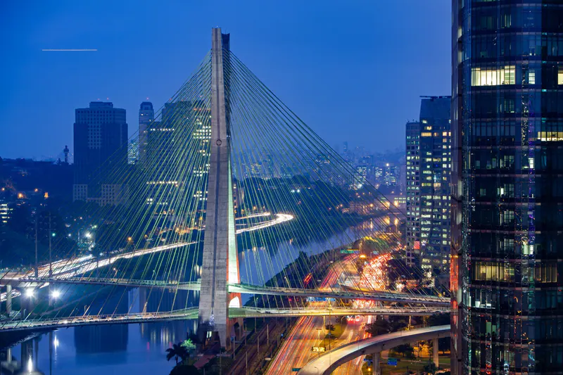 Cable-stayed bridge and illuminated roads among city towers at blue hour