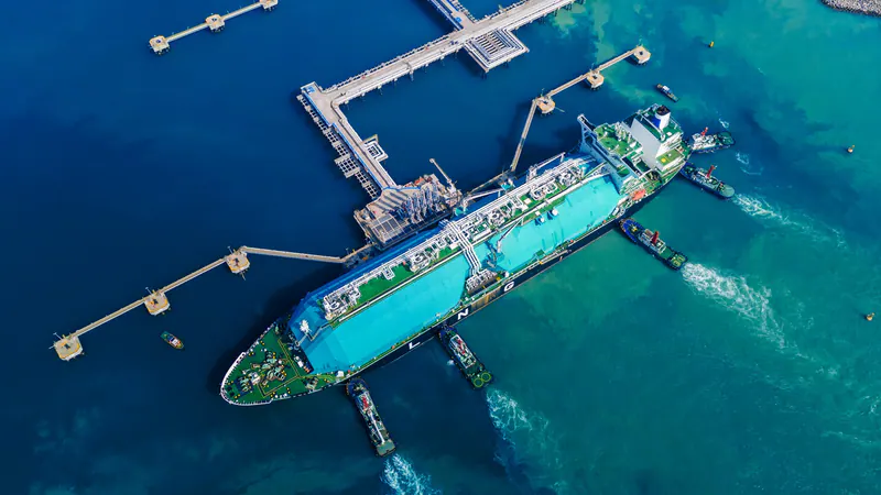 Aerial view of an LNG tanker and tugboats beside a marine terminal in blue water
