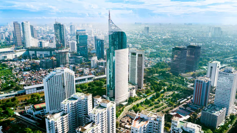 Aerial view of Jakarta city towers and green streets beneath a bright blue sky